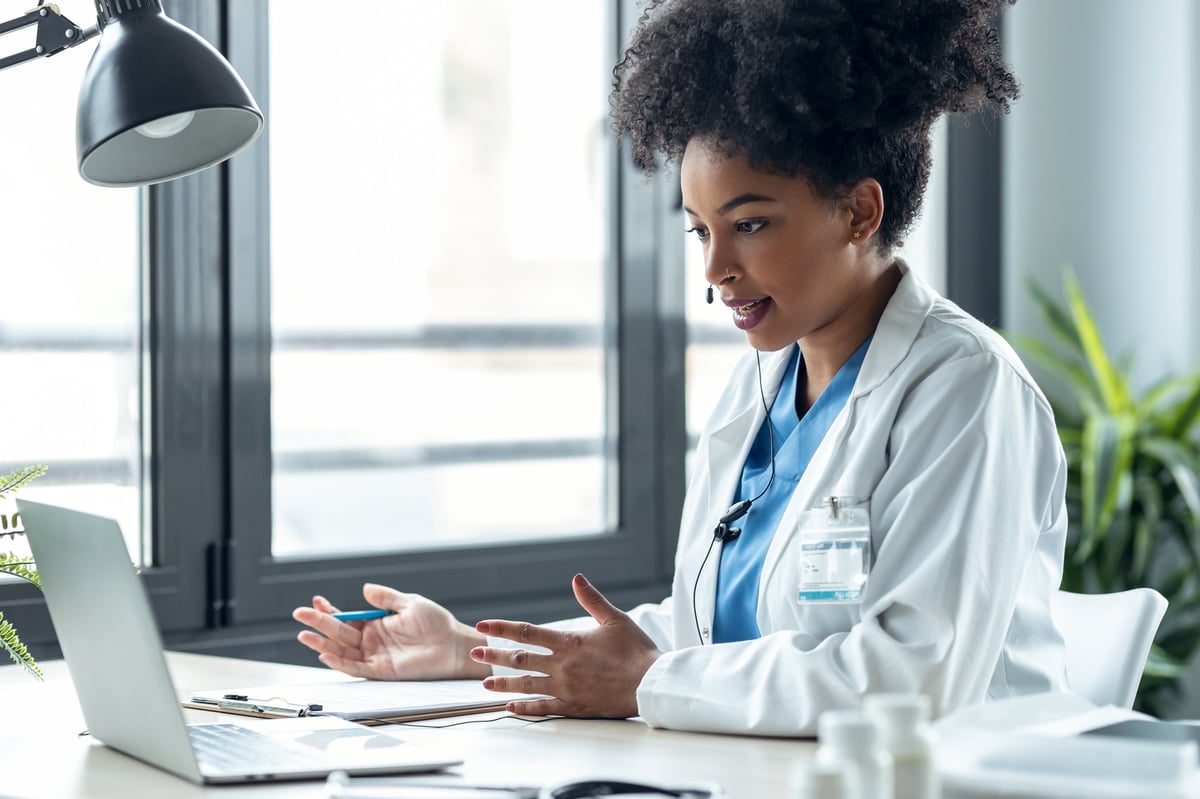 Shot of attractive afro female doctor talking while explaining medical treatment to patient through a video call with laptop in the consultation.